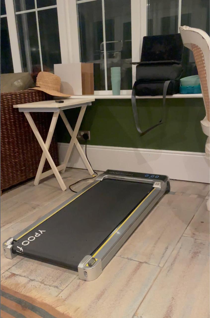 The walking pad set up against the window — the machine that lets you walk absolutely nowhere